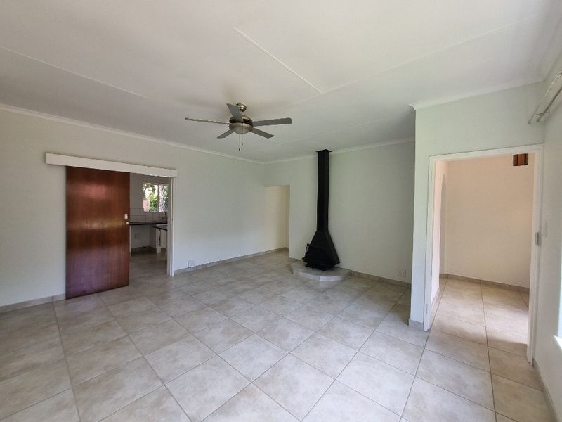 Spacious living area featuring neutral tiled flooring, a central ceiling fan, and a modern freestanding fireplace, offering a clean and versatile layout.