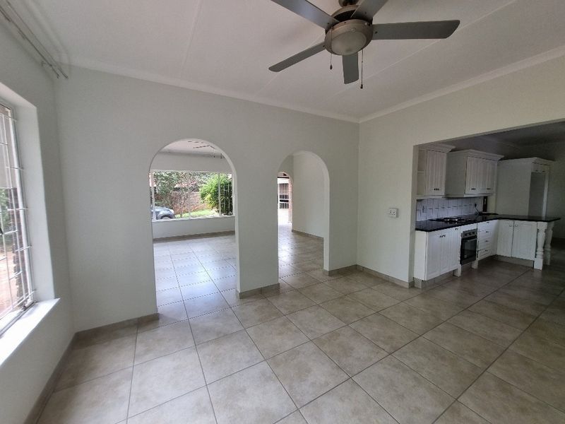 An open-plan living and kitchen area featuring tiled floors, arched architectural details, a ceiling fan, and a functional kitchen with built-in cabinetry.