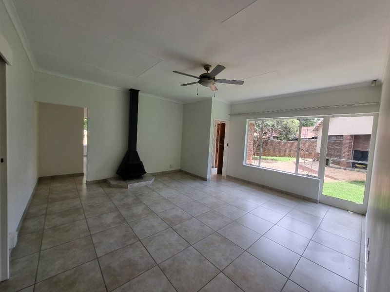 Spacious living area featuring neutral tiled flooring, a built-in fireplace, ceiling fan, and large windows providing natural light and garden access.