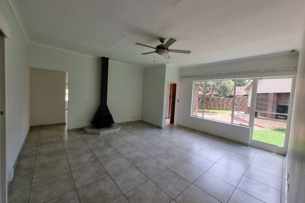 Spacious living area featuring neutral tiled flooring, a built-in fireplace, ceiling fan, and large windows providing natural light and garden access.