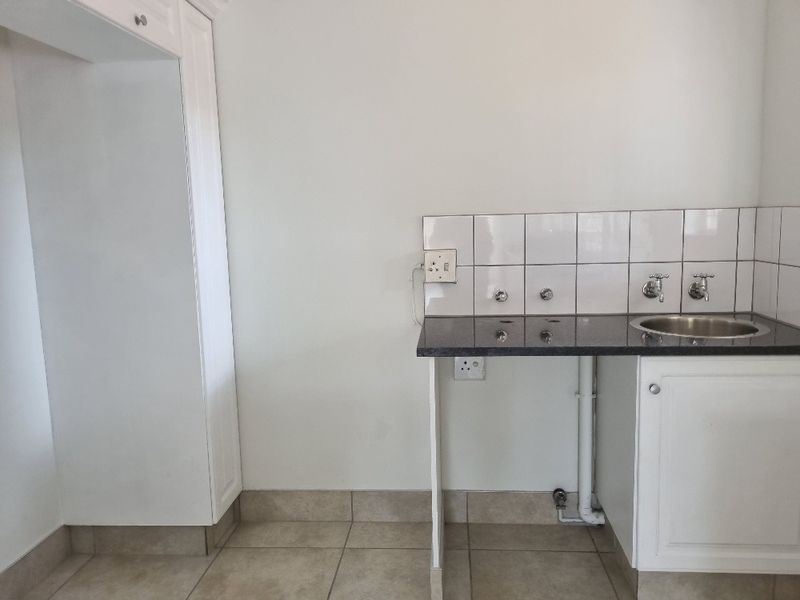 A clean and functional laundry area featuring built-in cabinetry, a granite countertop with a stainless steel sink, and tiled backsplash.