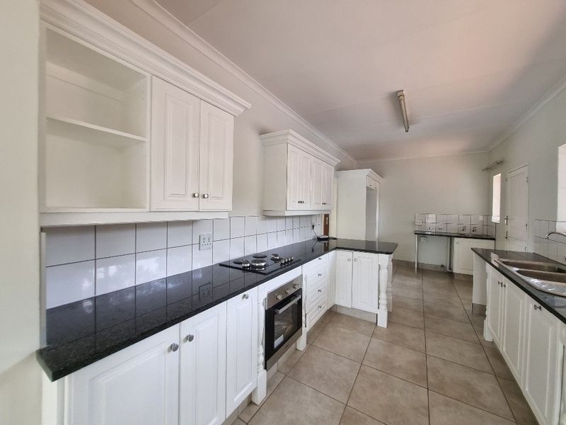 Spacious kitchen featuring white cabinetry, dark granite countertops, built-in oven, gas hob, and tiled flooring in a clean, neutral setting.