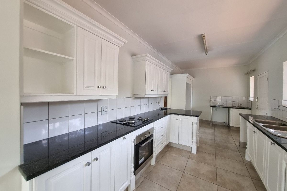 Spacious kitchen featuring white cabinetry, dark granite countertops, built-in oven, gas hob, and tiled flooring in a clean, neutral setting.
