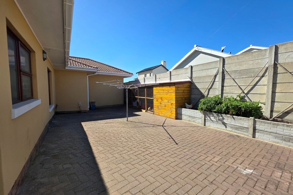 A paved rear courtyard featuring a precast concrete boundary wall, a raised brick planter, and a rotary clothesline.