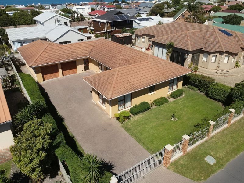 Aerial view of a residential property featuring a tiled roof, double garage, paved driveway, and a well-maintained front lawn with perimeter fencing.