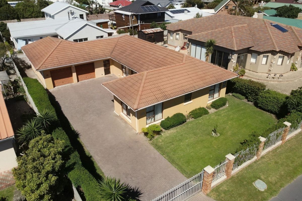 Aerial view of a residential property featuring a tiled roof, double garage, paved driveway, and a well-maintained front lawn with perimeter fencing.