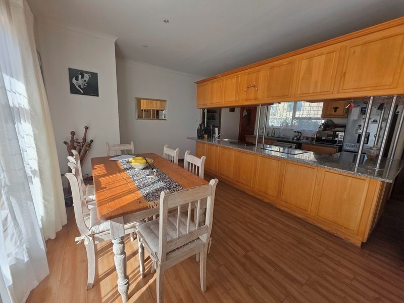 Open plan kitchen and dining area featuring warm wooden cabinetry, granite countertops, and laminate flooring, creating a functional and connected living space.