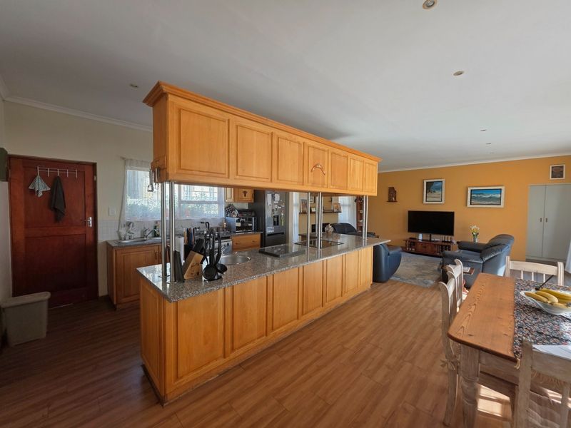 Open-plan living area featuring a large kitchen island with granite countertops, wooden cabinetry, and integrated hob, flowing into a spacious lounge and dining area.