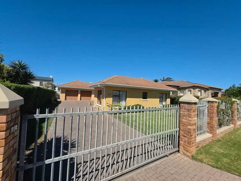 Front view of a single-story house featuring a paved driveway, double garage, and a secure gated entrance with a well-maintained lawn.