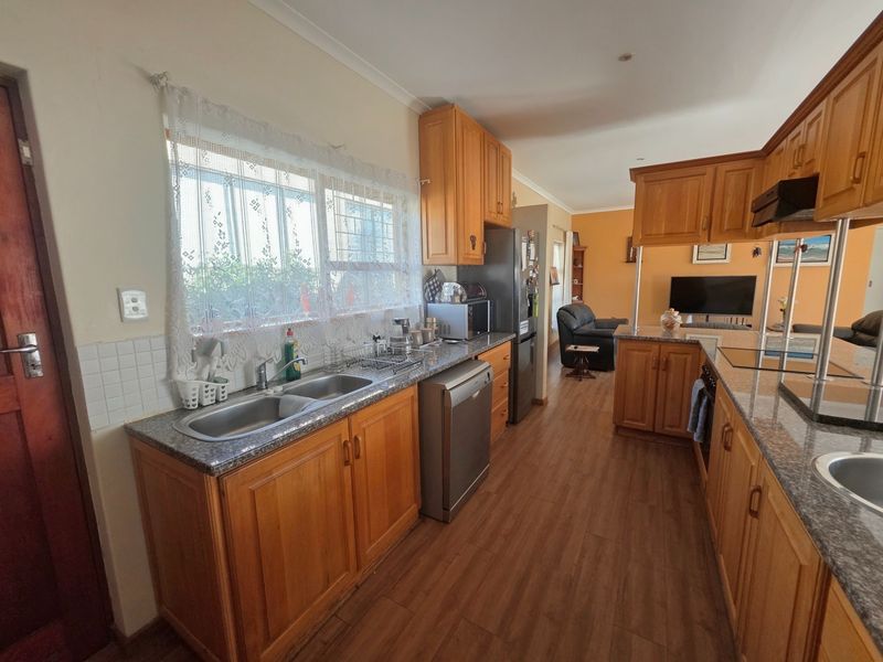 Open plan kitchen featuring wooden cabinetry, granite countertops, and a double bowl sink, flowing into a living area with laminate flooring.
