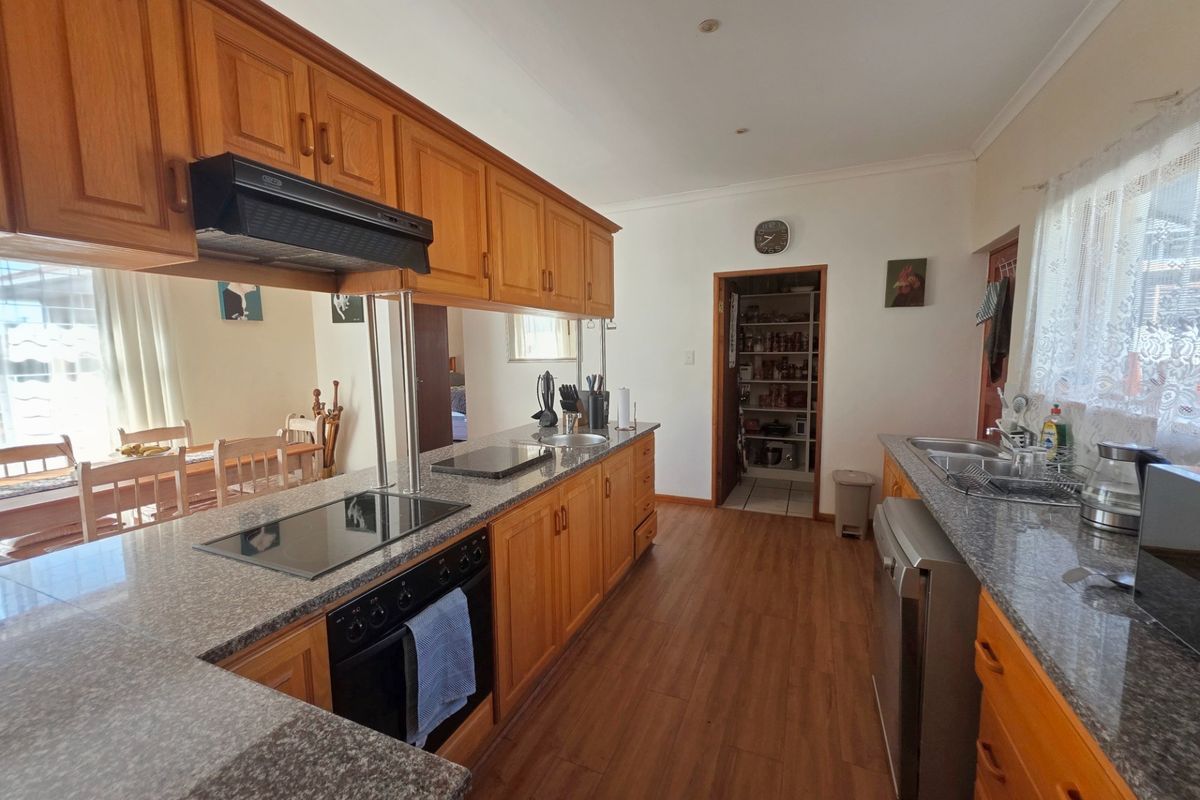 A functional kitchen featuring wooden cabinetry, granite countertops, built-in oven, electric hob, and an adjacent pantry area with laminate flooring.