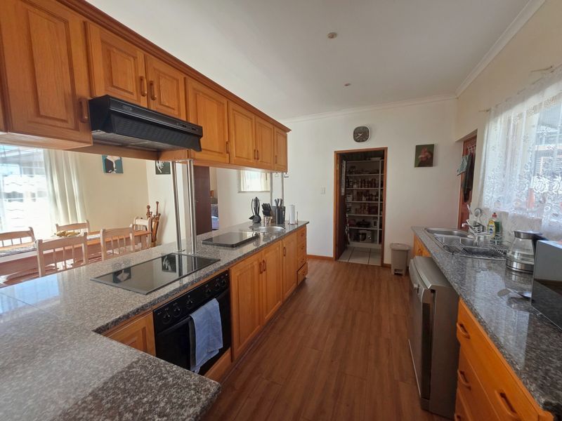 A functional kitchen featuring wooden cabinetry, granite countertops, built-in oven, electric hob, and an adjacent pantry area with laminate flooring.