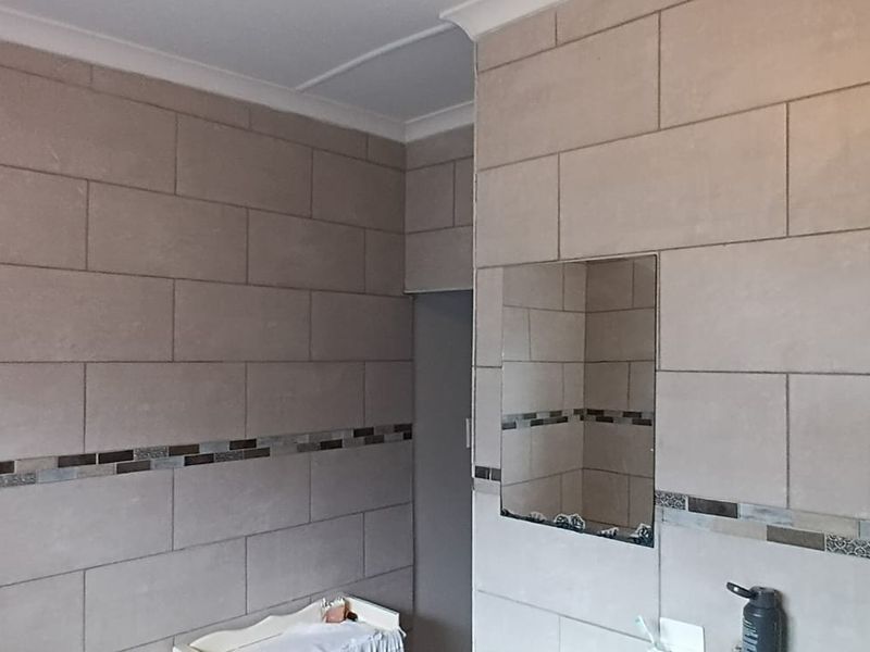 A clean bathroom featuring neutral large-format wall tiles with a decorative mosaic border, a wall-mounted mirror, and a modern shower head.