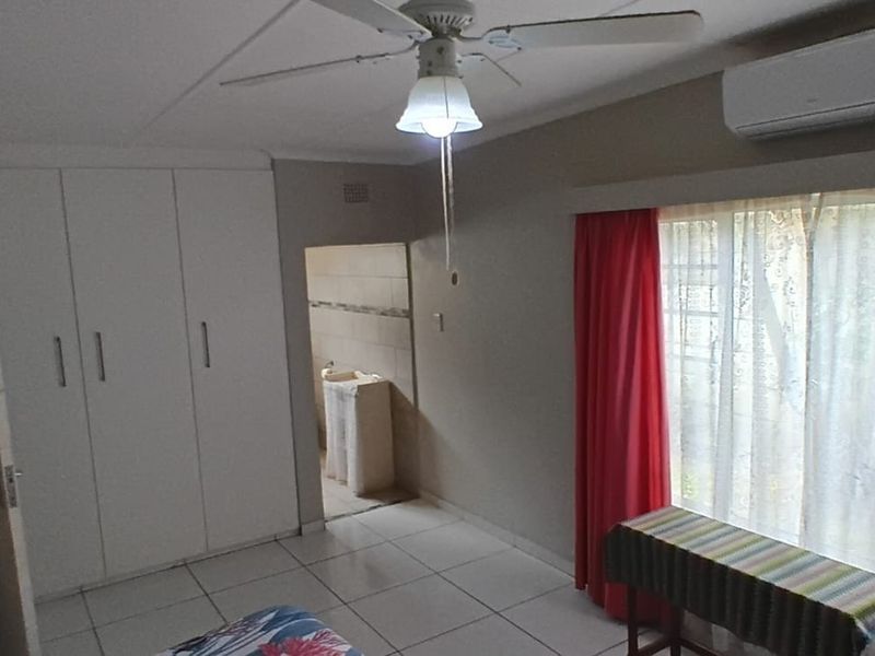 Bedroom featuring built-in cupboards, tiled flooring, a ceiling fan, and a wall-mounted air conditioning unit.