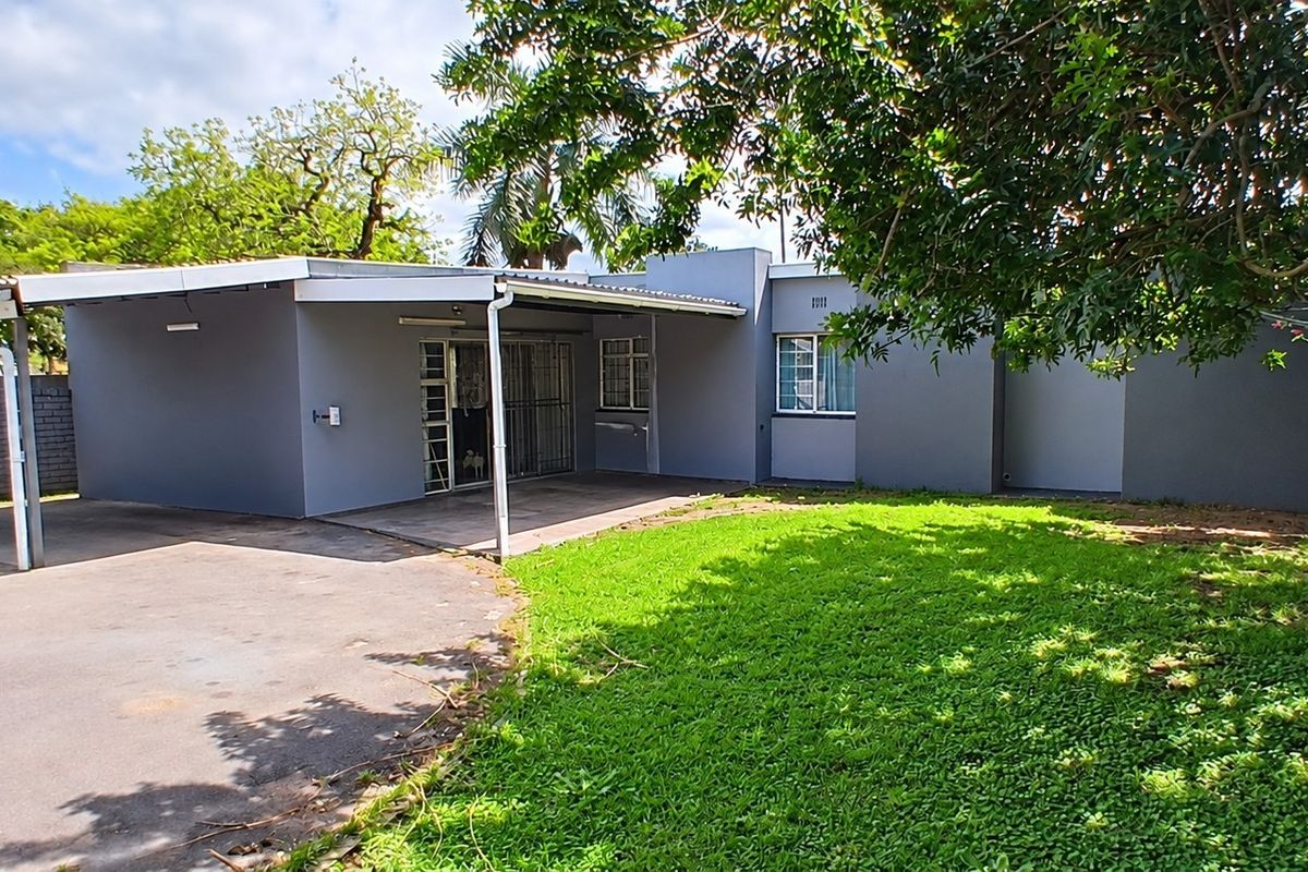 Rear view of the property featuring a covered patio area, paved driveway, and a well-maintained lawn with established trees.