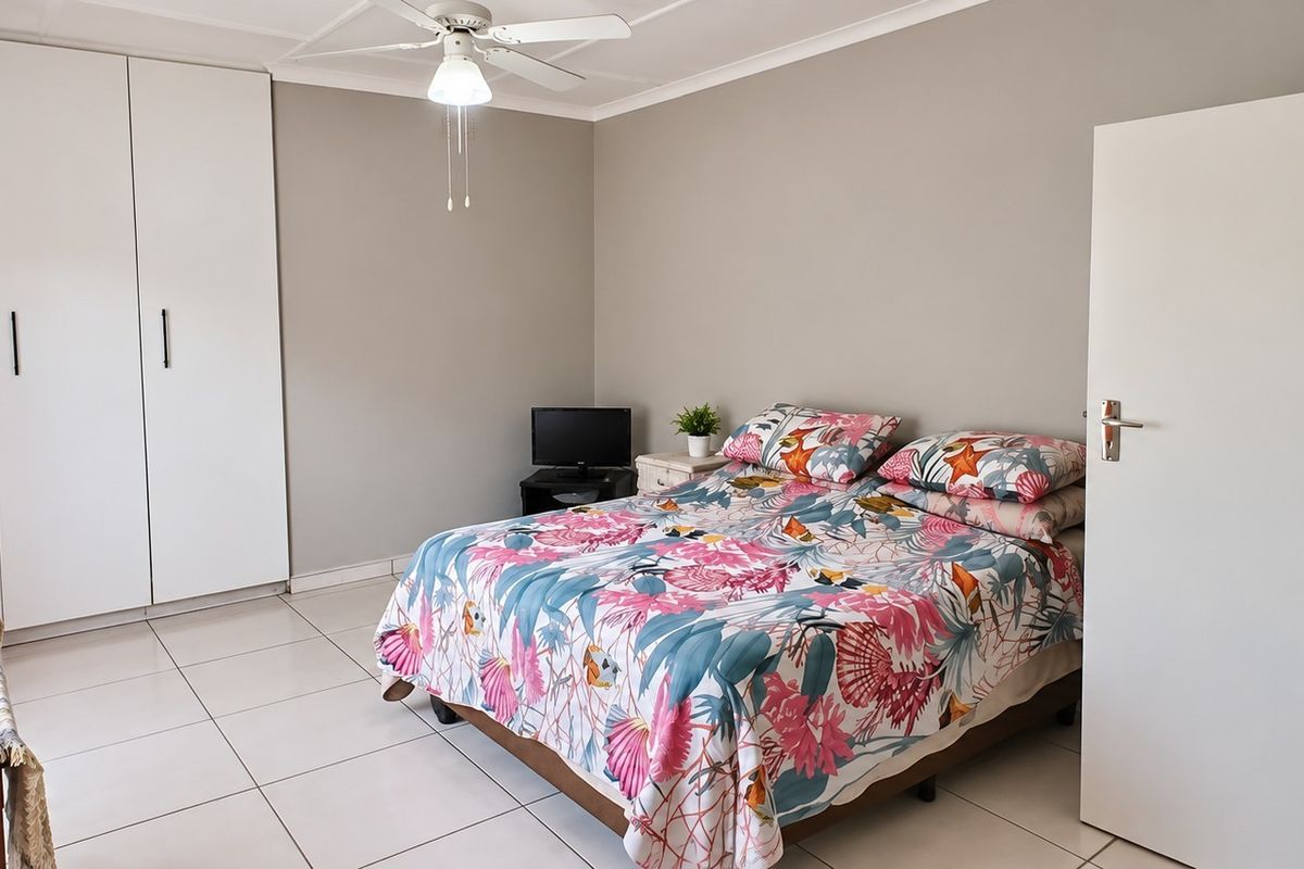 A well-lit bedroom featuring neutral wall tones, tiled flooring, a ceiling fan, and ample built-in cupboard storage.