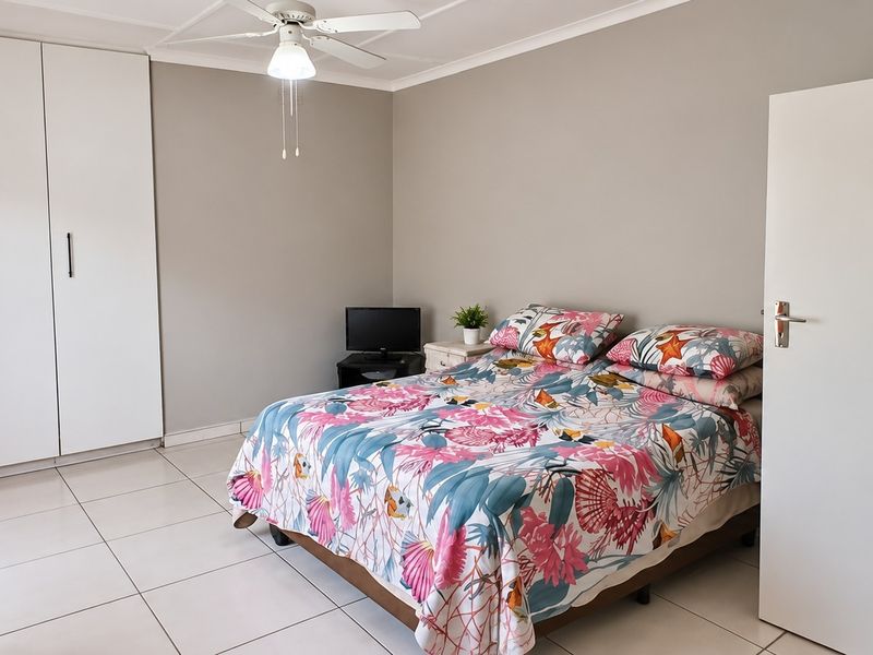 A well-lit bedroom featuring neutral wall tones, tiled flooring, a ceiling fan, and ample built-in cupboard storage.