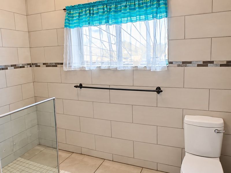 A clean, modern bathroom featuring neutral wall tiles with a mosaic accent border, a glass shower screen, and a standard toilet.