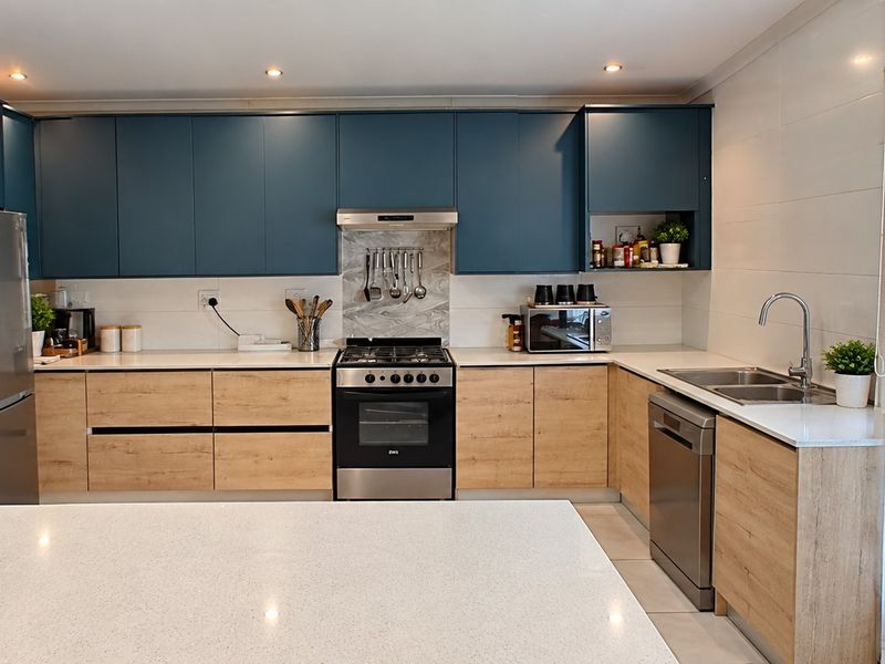 Modern kitchen featuring two-tone cabinetry, quartz countertops, gas stove with extractor, and direct access to the garden through sliding glass doors.