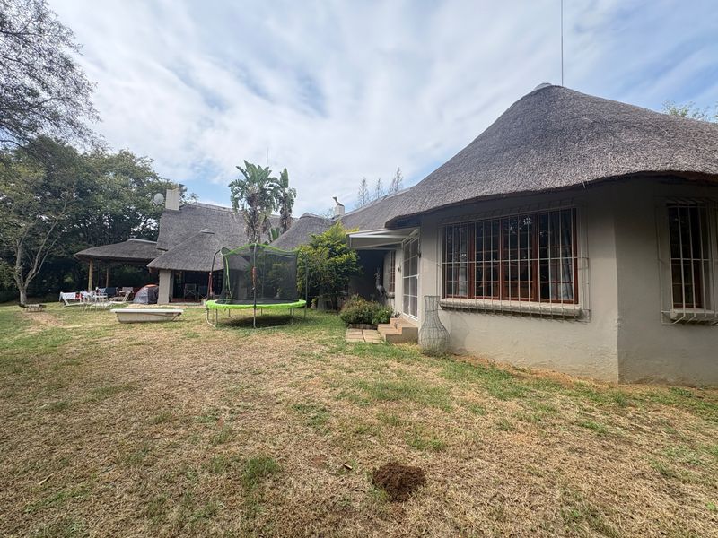 Rear view of a traditional thatched-roof small holding property featuring a spacious garden and a covered patio area.