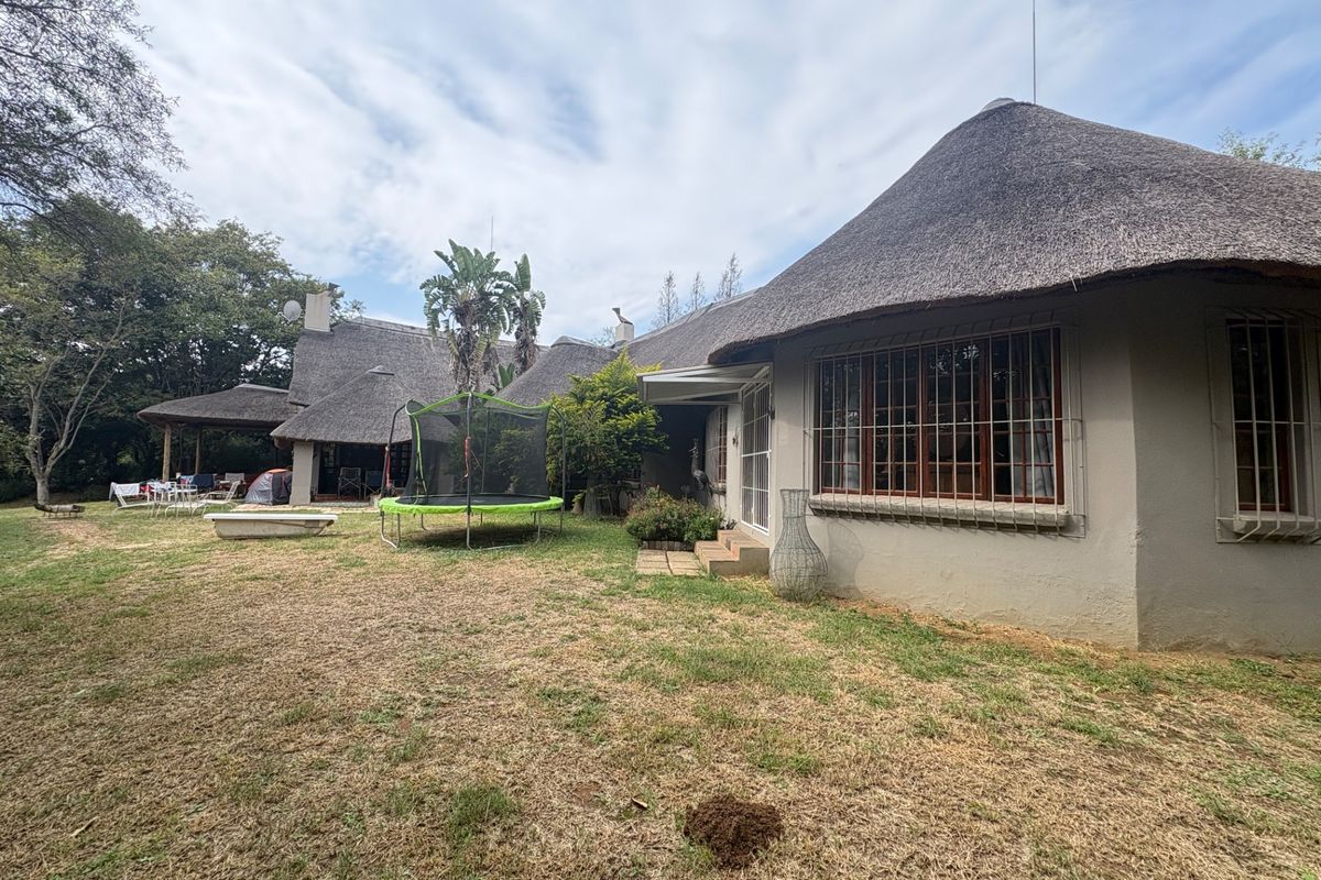 Rear view of a traditional thatched-roof small holding property featuring a spacious garden and a covered patio area.