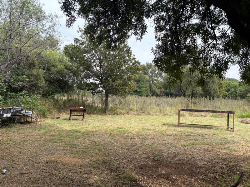A spacious, natural garden area featuring mature trees and open lawn space, offering a quiet outdoor setting on the small holding.
