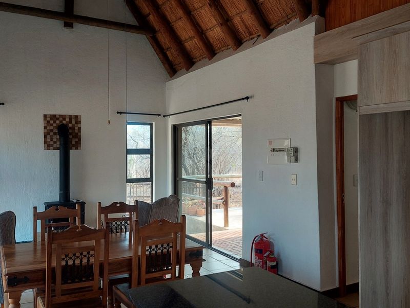 Open-plan living and dining area featuring a high thatched ceiling with exposed rafters, a freestanding fireplace, and sliding doors leading to an outdoor patio.
