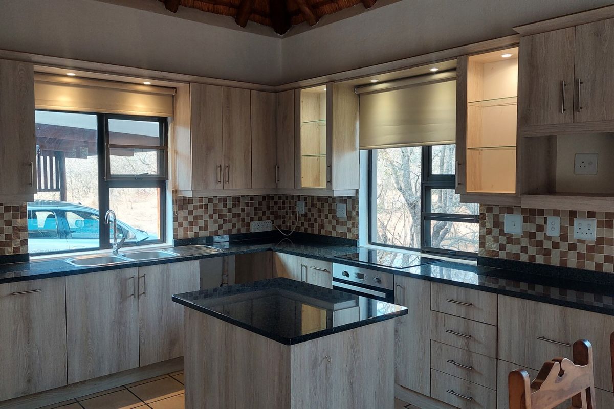 Modern kitchen featuring light wood-grain cabinetry, dark granite countertops, a central island, and a mosaic tile backsplash with integrated appliances.