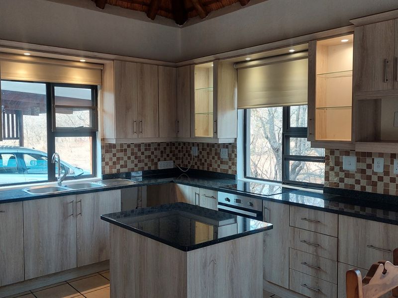 Modern kitchen featuring light wood-grain cabinetry, dark granite countertops, a central island, and a mosaic tile backsplash with integrated appliances.