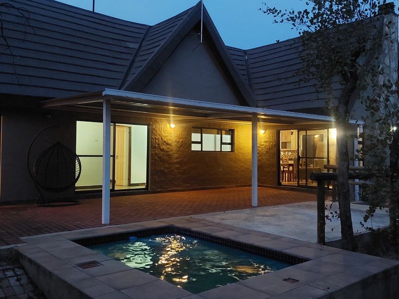 Rear view of the house featuring a covered patio, paved outdoor area, and a built-in plunge pool at dusk.
