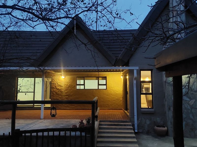 Rear elevation of the house featuring a covered patio, brick paving, stone cladding accents, and exterior lighting at dusk.