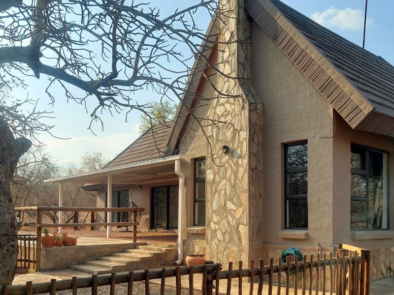 Rear view of a house featuring a stone chimney, tiled roof, and a covered patio area with timber railings.