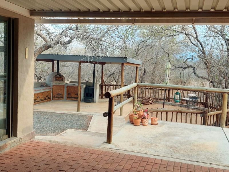 Spacious covered patio featuring a built-in braai and pizza oven, overlooking a natural bushveld setting with timber railings and paved flooring.