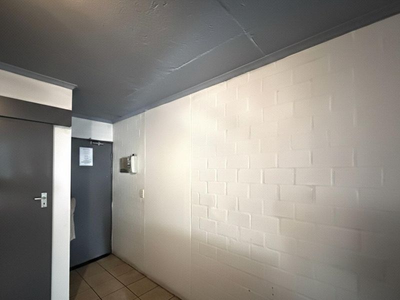 A functional hallway featuring tiled flooring, a painted brick feature wall, and an integrated intercom system.