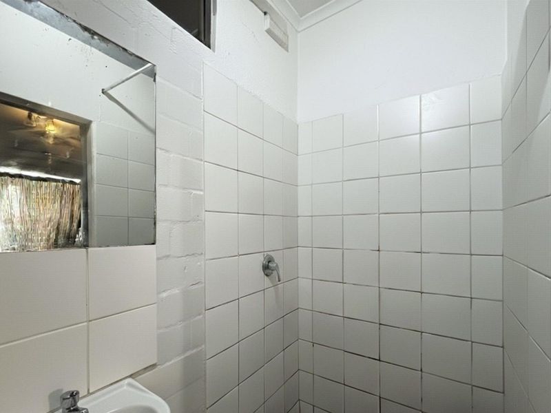A functional bathroom featuring a tiled shower enclosure, basin with mixer tap, and wall-mounted mirror, requiring cosmetic updates to the tiling and finishes.