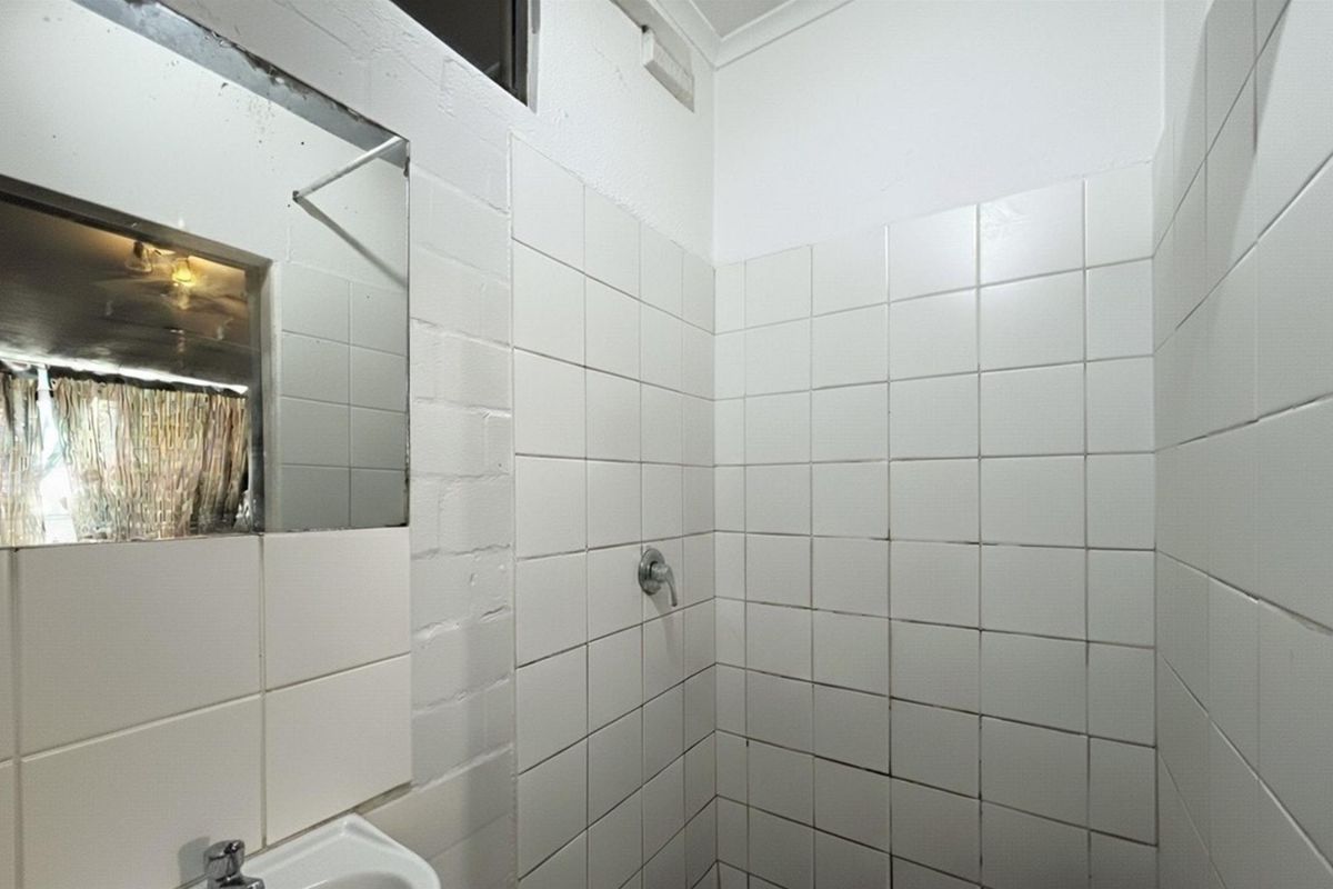 A functional bathroom featuring a tiled shower enclosure, basin with mixer tap, and wall-mounted mirror, requiring cosmetic updates to the tiling and finishes.