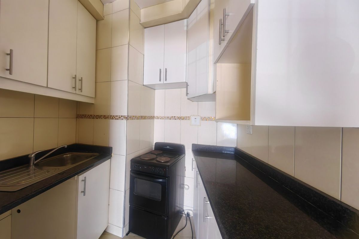 Compact kitchen featuring granite countertops, built-in cabinetry, tiled backsplash, and a freestanding stove, offering a functional layout for an apartment.