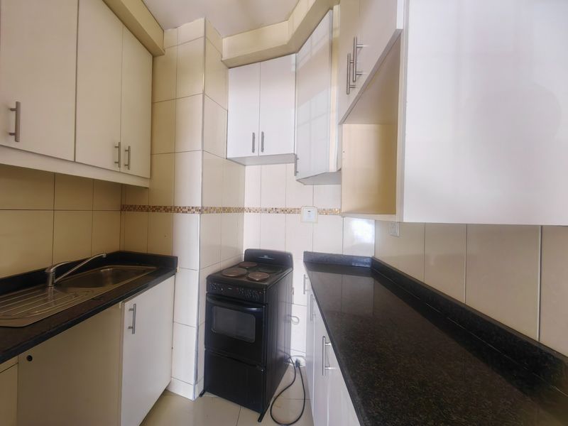 Compact kitchen featuring granite countertops, built-in cabinetry, tiled backsplash, and a freestanding stove, offering a functional layout for an apartment.
