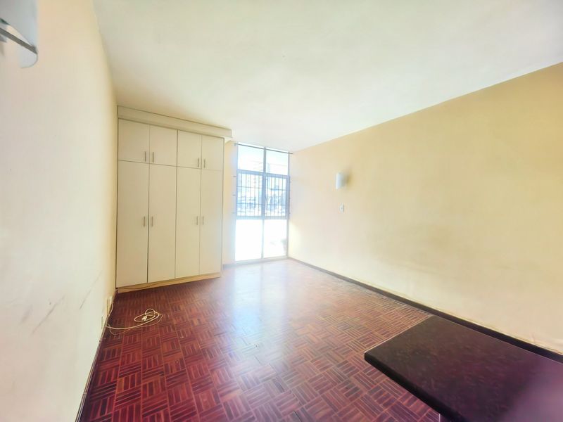 An empty bedroom featuring parquet flooring, built-in cupboards, and a window with a security gate, offering a blank canvas for personalization.
