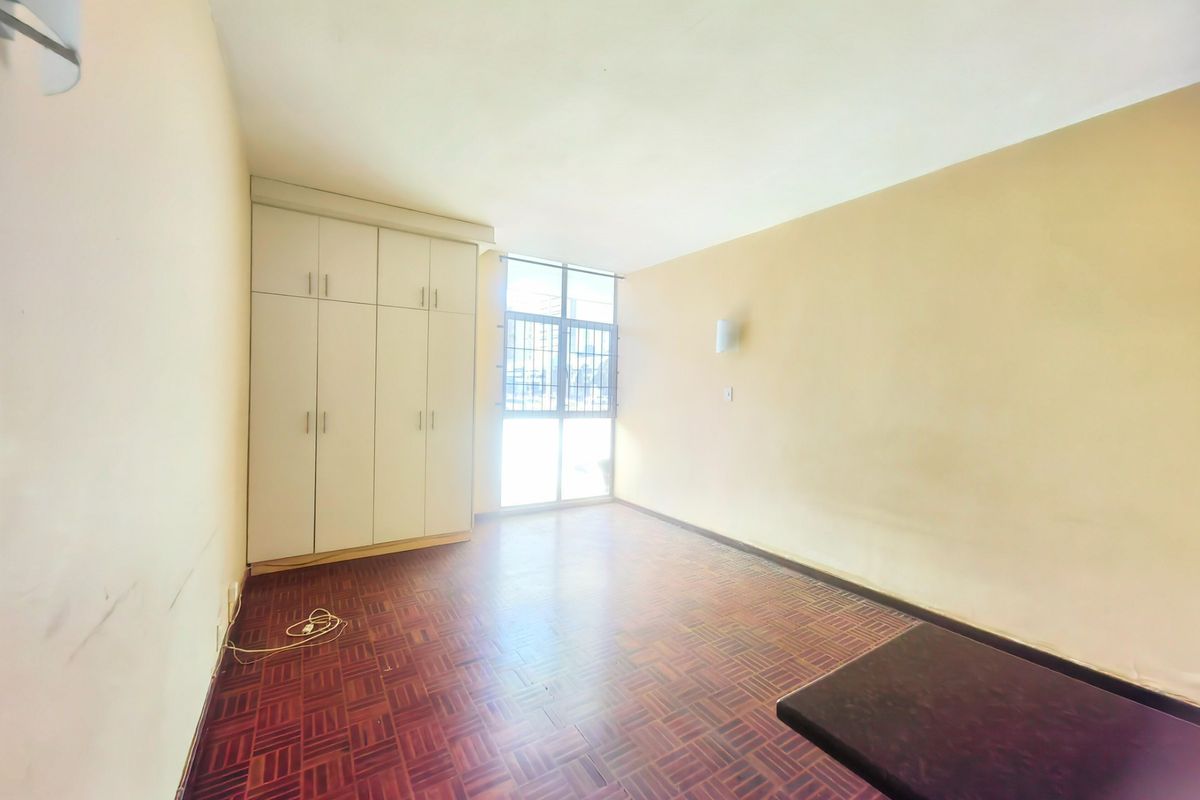 An empty bedroom featuring parquet flooring, built-in cupboards, and a window with a security gate, offering a blank canvas for personalization.