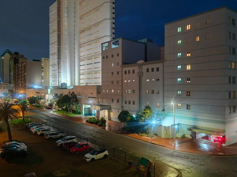 Night view of the apartment building exterior, featuring a paved parking area, building facade, and exterior lighting.