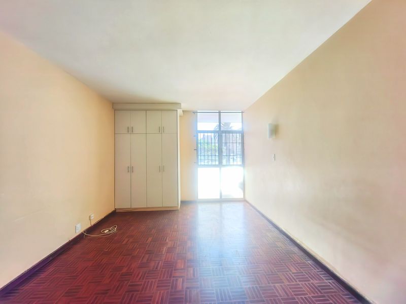 An empty bedroom featuring parquet flooring, built-in cupboards, and a sliding door with security bars providing natural light.