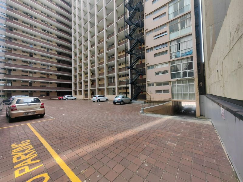 A view of the rear exterior of a multi-story apartment building featuring a paved parking area and an external fire escape staircase.