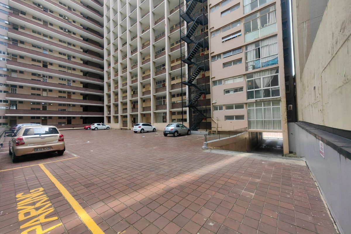A view of the rear exterior of a multi-story apartment building featuring a paved parking area and an external fire escape staircase.
