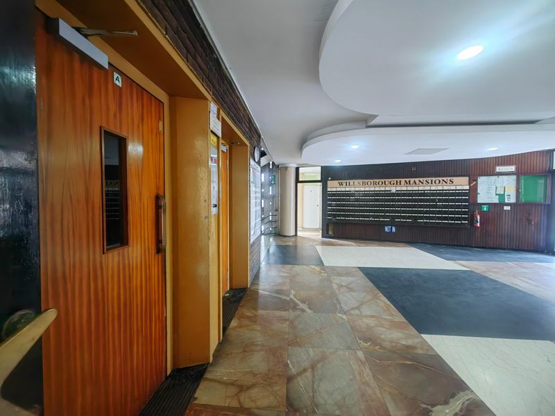 Spacious apartment building entrance lobby featuring elevator access, integrated mailboxes, and decorative wood paneling with recessed ceiling lighting.