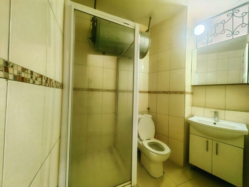 A functional bathroom featuring a shower enclosure, toilet, and vanity basin with integrated storage, finished with neutral wall tiling.