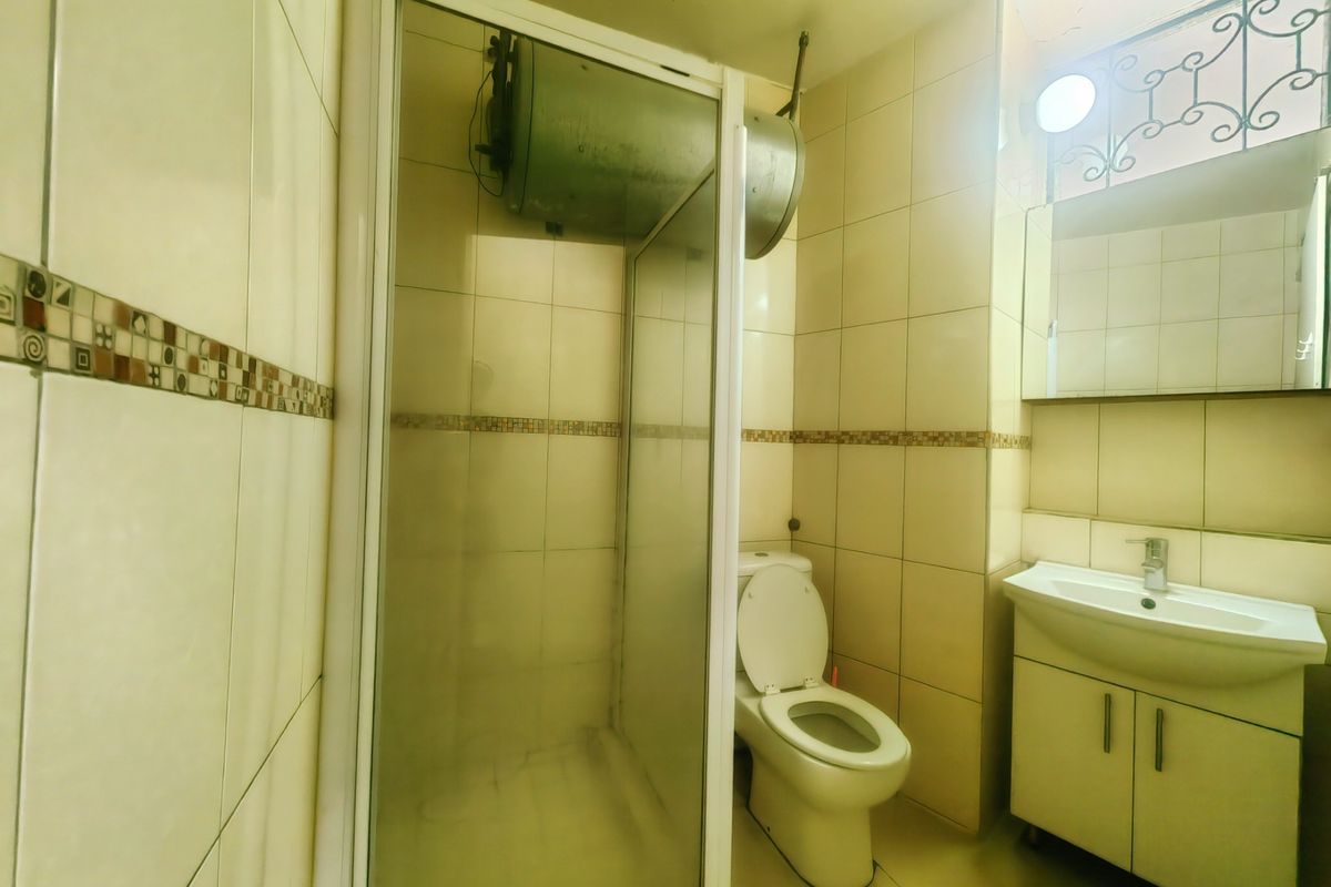 A functional bathroom featuring a shower enclosure, toilet, and vanity basin with integrated storage, finished with neutral wall tiling.
