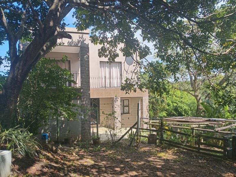 Rear view of a two-story house featuring a balcony, stone cladding accents, and a fenced garden area surrounded by mature trees.