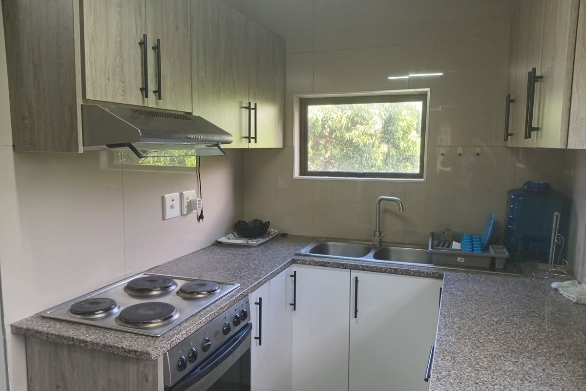 A functional kitchen featuring modern wood-look cabinetry, granite-style countertops, a built-in electric stove with extractor fan, and a double basin sink.