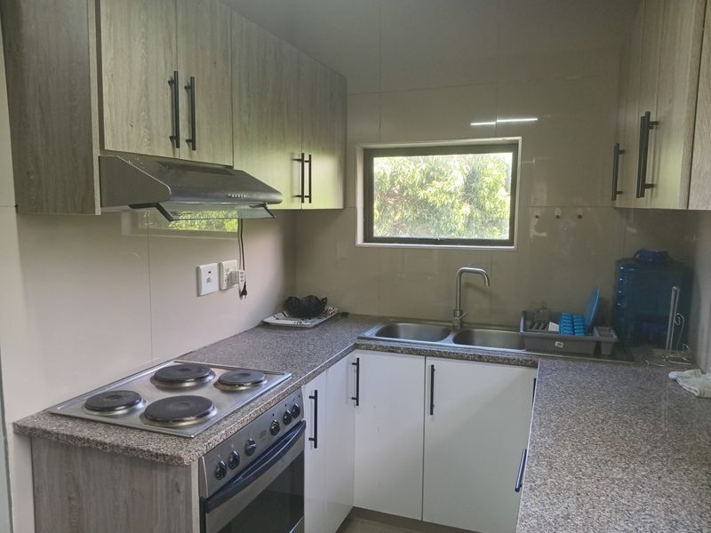 A functional kitchen featuring modern wood-look cabinetry, granite-style countertops, a built-in electric stove with extractor fan, and a double basin sink.